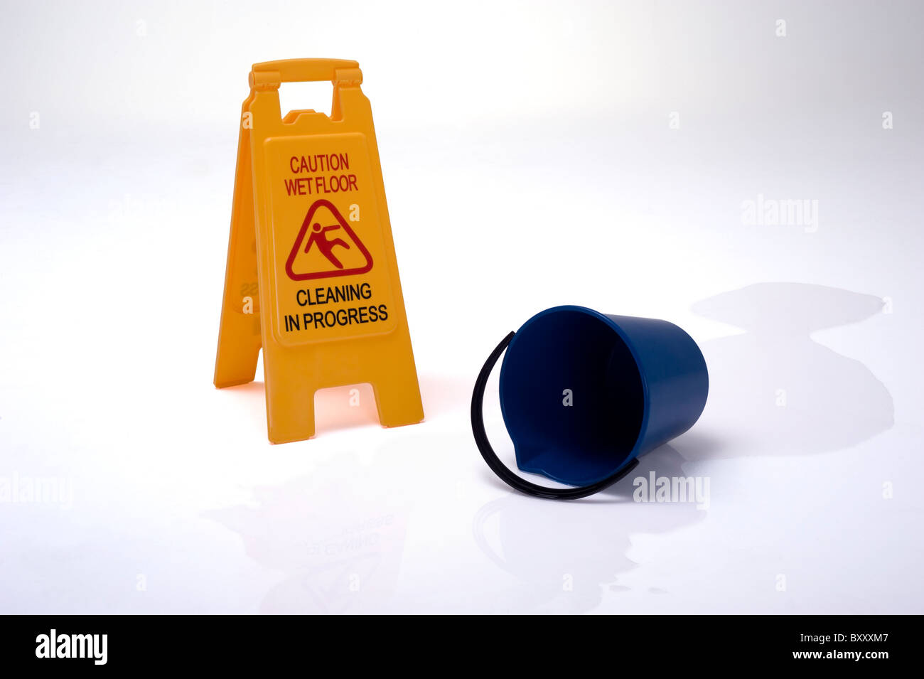 Acqua versata dalla benna blu sul pavimento accanto a un segnale di avvertimento pavimento bagnato. Foto Stock