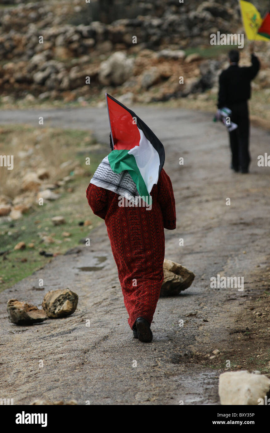 La donna palestinese cammina con la bandiera palestinese durante un rally settimanale contro la costruzione delle barriere di separazione controverse che Israele sta costruendo nel villaggio della Cisgiordania di Bil'in Israele Foto Stock