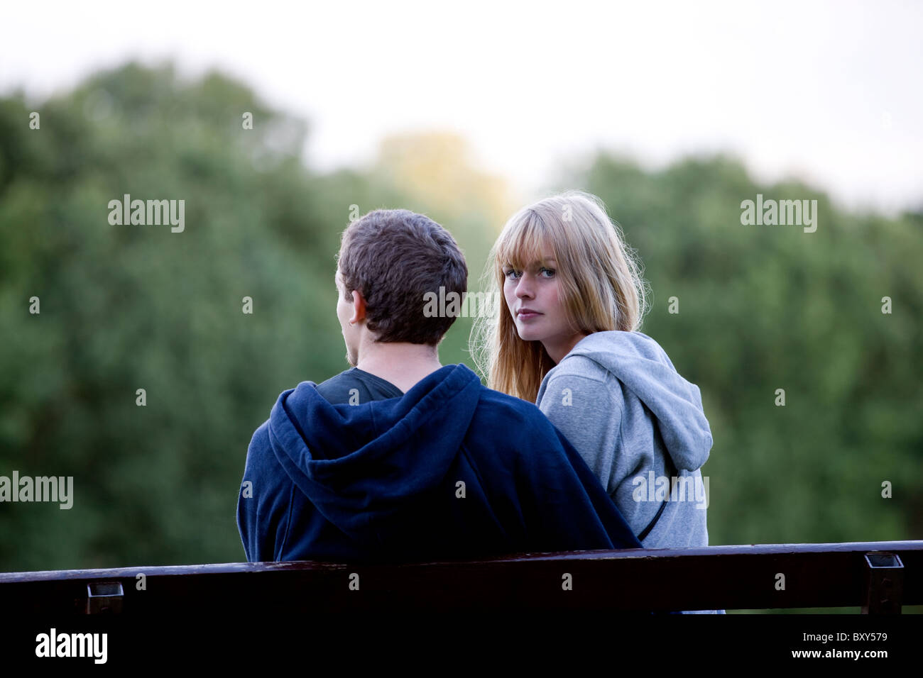 Vista posteriore di una giovane coppia su un banco, una donna che guarda la fotocamera Foto Stock