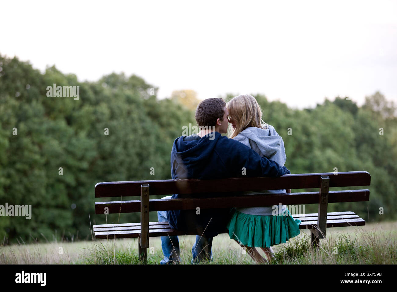 Vista posteriore di un romantico di coppia giovane su una panchina nel parco Foto Stock
