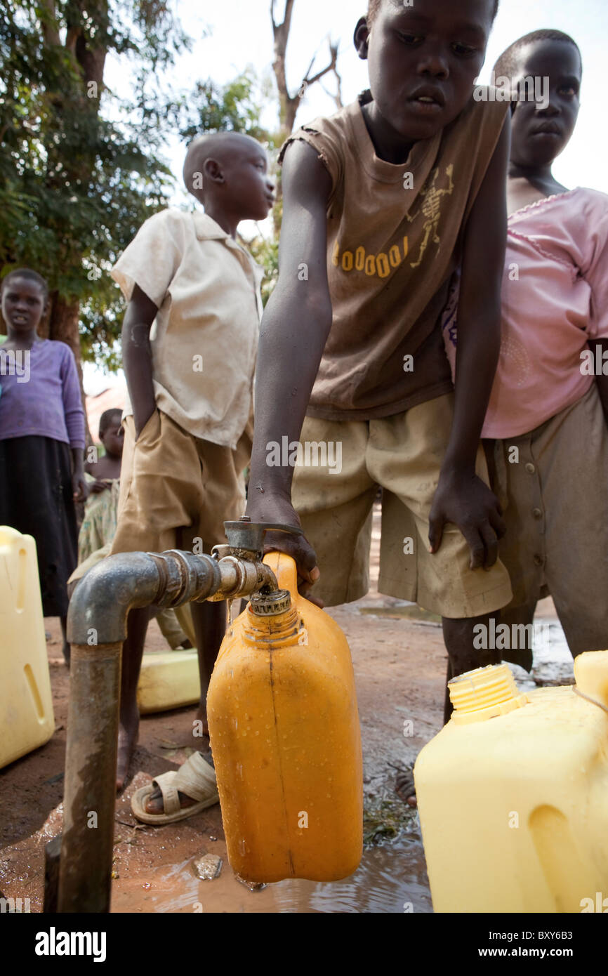 I bambini riempiono taniche di acqua da un rubinetto esterno Amuria Centro Salute IV - Quartiere Amuria, Uganda, Africa orientale. Foto Stock