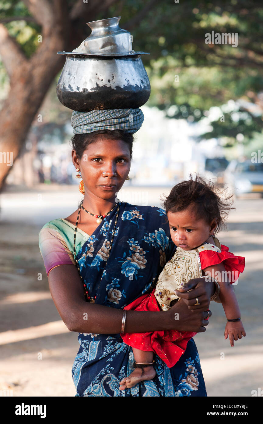 Poveri di casta inferiore donna indiana con il bambino che porta un piatto di riso sul suo capo. Andhra Pradesh, India Foto Stock