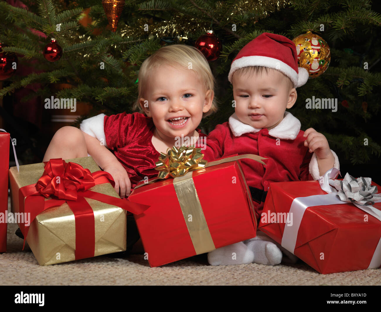 Due anno vecchia ragazza e un ottavo mese vecchio ragazzo seduto con presenta sotto un albero di Natale Foto Stock