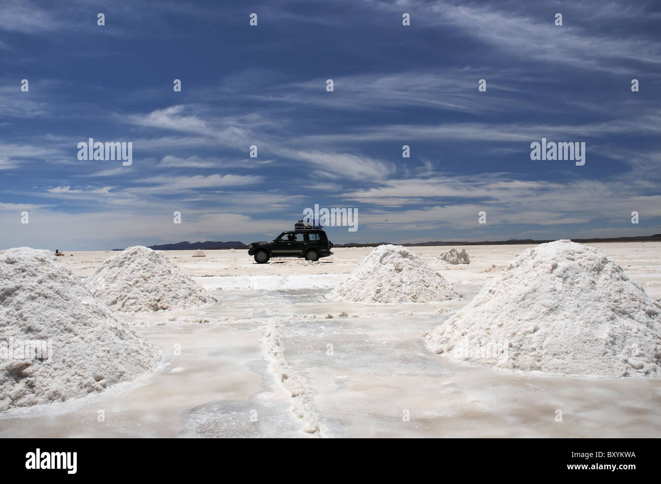 Un veicolo che attraversa il Salar de Uyuni tra pile di sale scavata e pronto per la purificazione Foto Stock