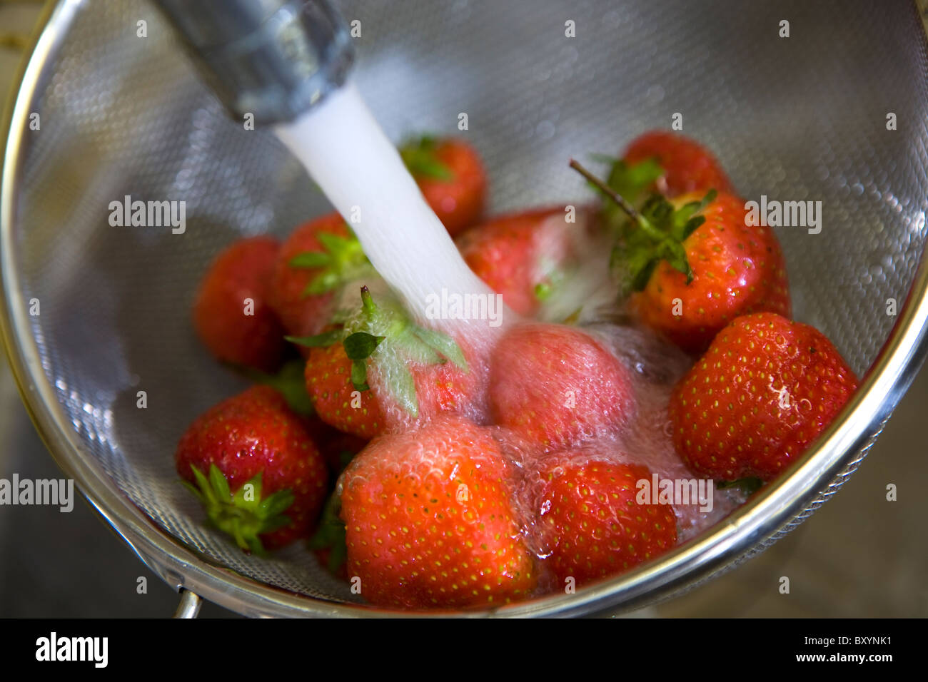 Le fragole di essere lavati in un vaglio metallico con acqua del rubinetto Foto Stock