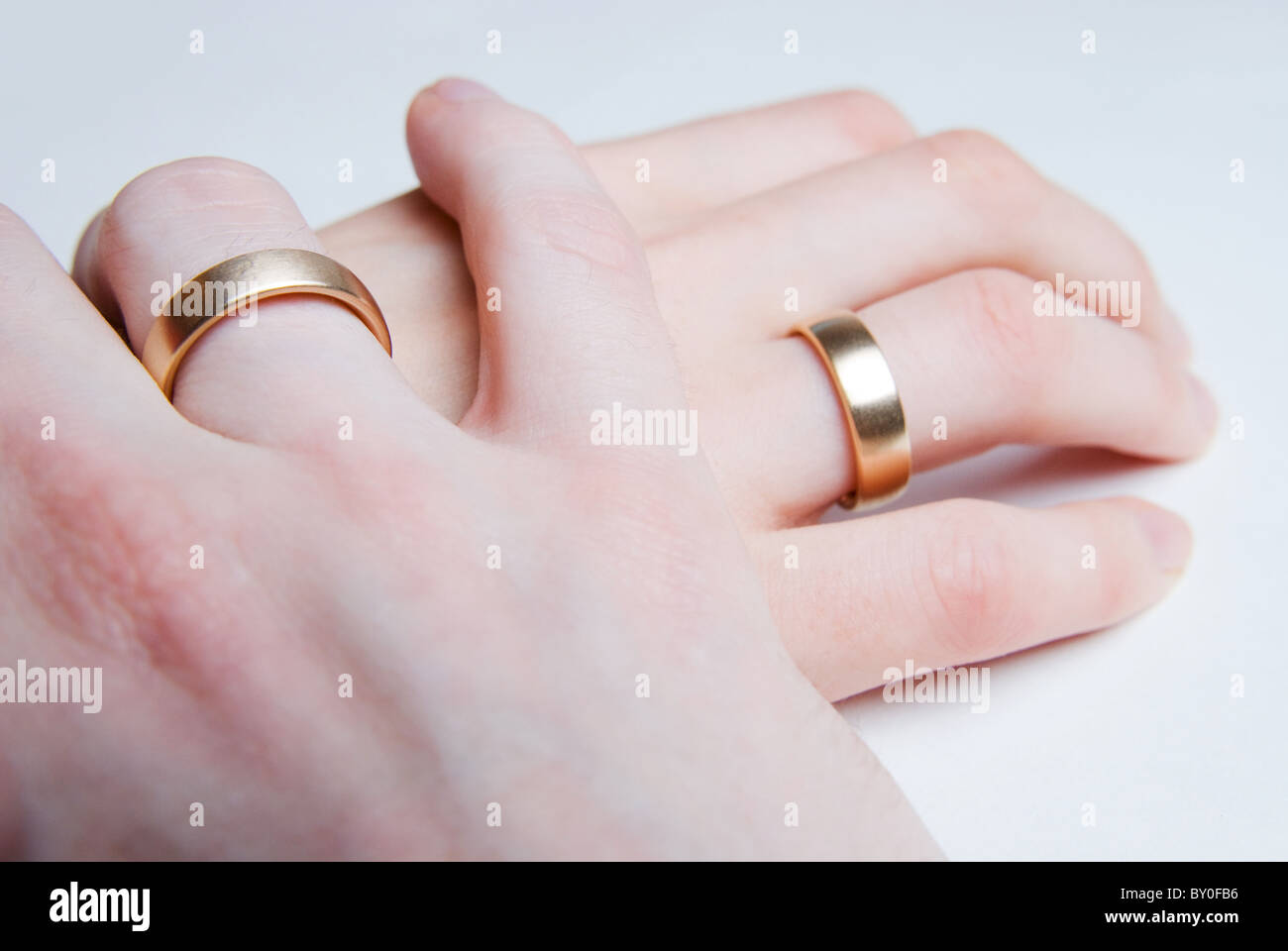 La mano di un uomo è dolcemente tenendo per mano di una donna, entrambi indossando golden gli anelli di nozze Foto Stock