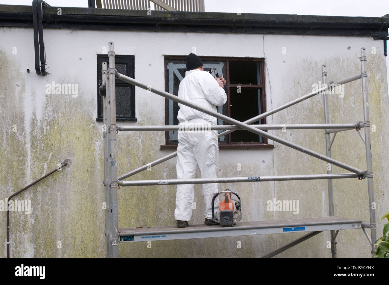 Un Builder consente di rimuovere una vecchia finestra mentre in piedi sul ponteggio Foto Stock