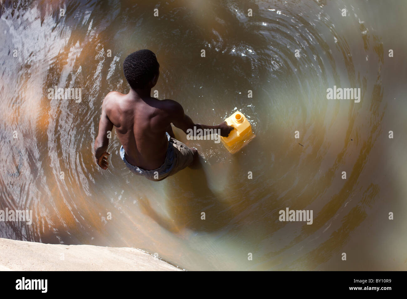MECEBURI riserva forestale, nei pressi di Nampula, Mozambico, Maggio 2010 : un abitante di un villaggio riempie il contenitore con acqua nel flusso locale. Foto Stock