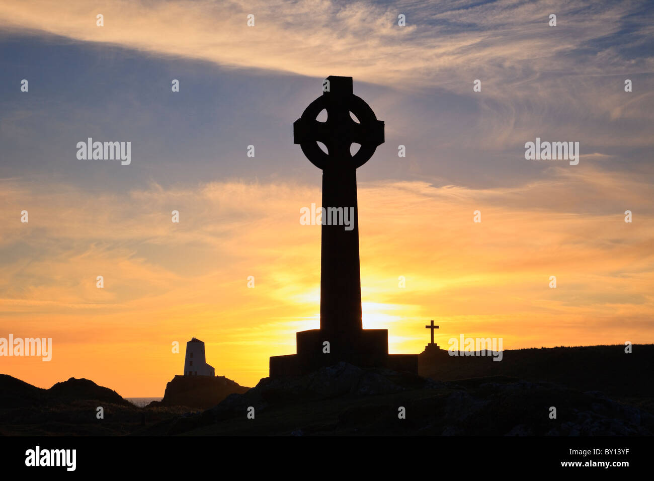 Tramonto dietro San Dwynwen's Celtic cross e Twr Mawr faro in silhouette sull isola di Llanddwyn. Newborough, Isola di Anglesey, Galles del Nord, Regno Unito Foto Stock