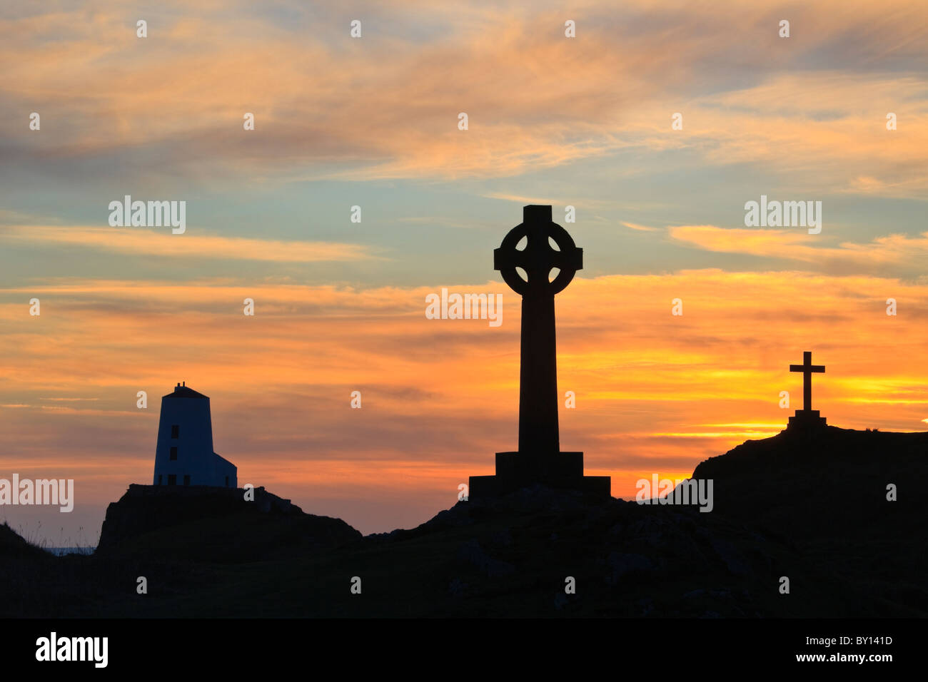 St Dwynwen croce celtica e Twr Mawr faro in silhouette sull isola di Llanddwyn al tramonto / Tramonto. Isola di Anglesey North Wales UK Gran Bretagna Foto Stock
