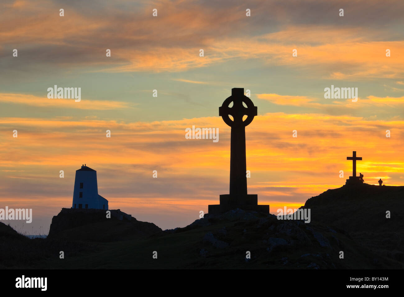 St Dwynwen croce celtica e Twr Mawr faro in silhouette sull isola di Llanddwyn al tramonto Isola di Anglesey, Galles del Nord, Regno Unito Foto Stock