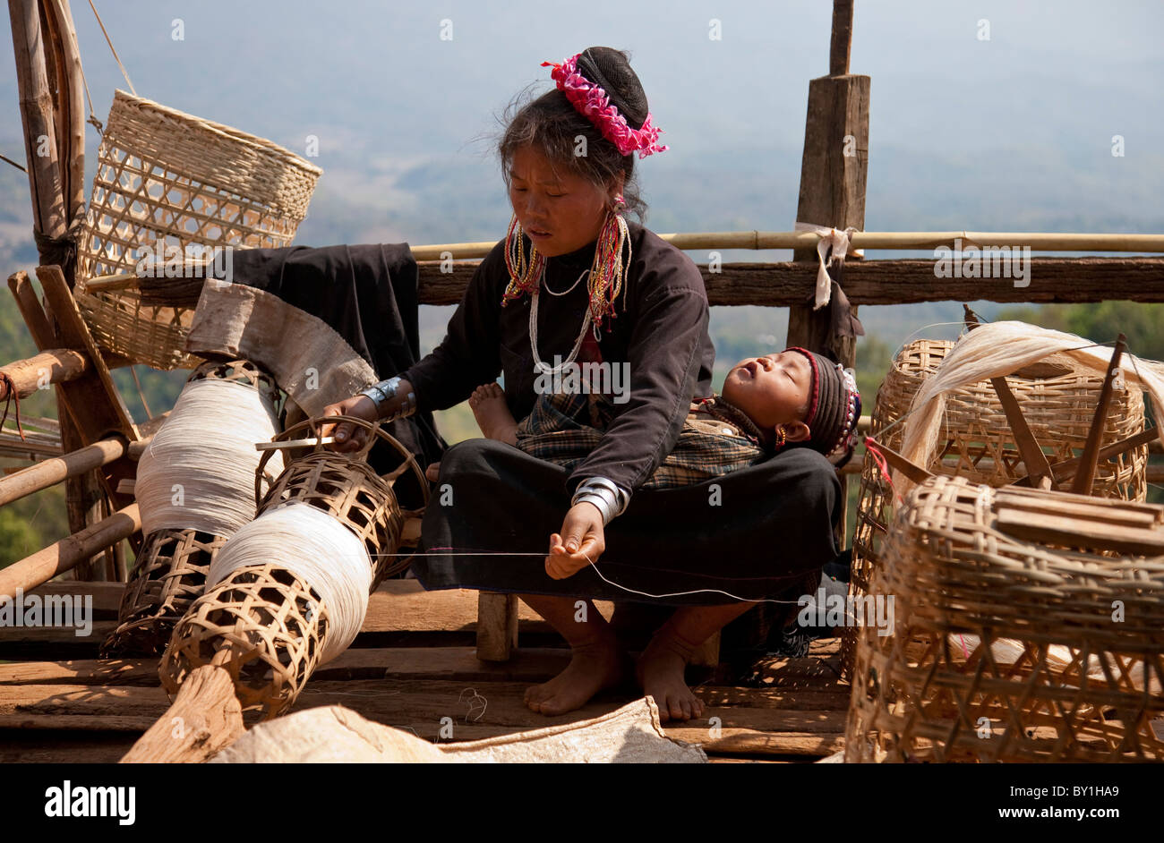 Myanmar Birmania, Keng Tung (Kyaing Tong). Un Ann (ENN) lady thread di filatura sulla piattaforma di casa sua, con il suo bambino Foto Stock