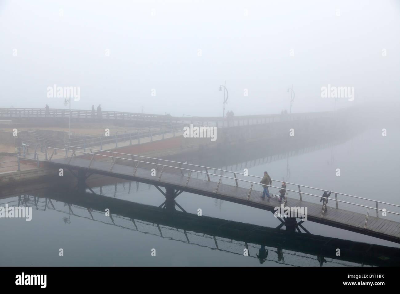 Passerella Pedonale su acqua con persone che attraversano in un giorno di nebbia Foto Stock