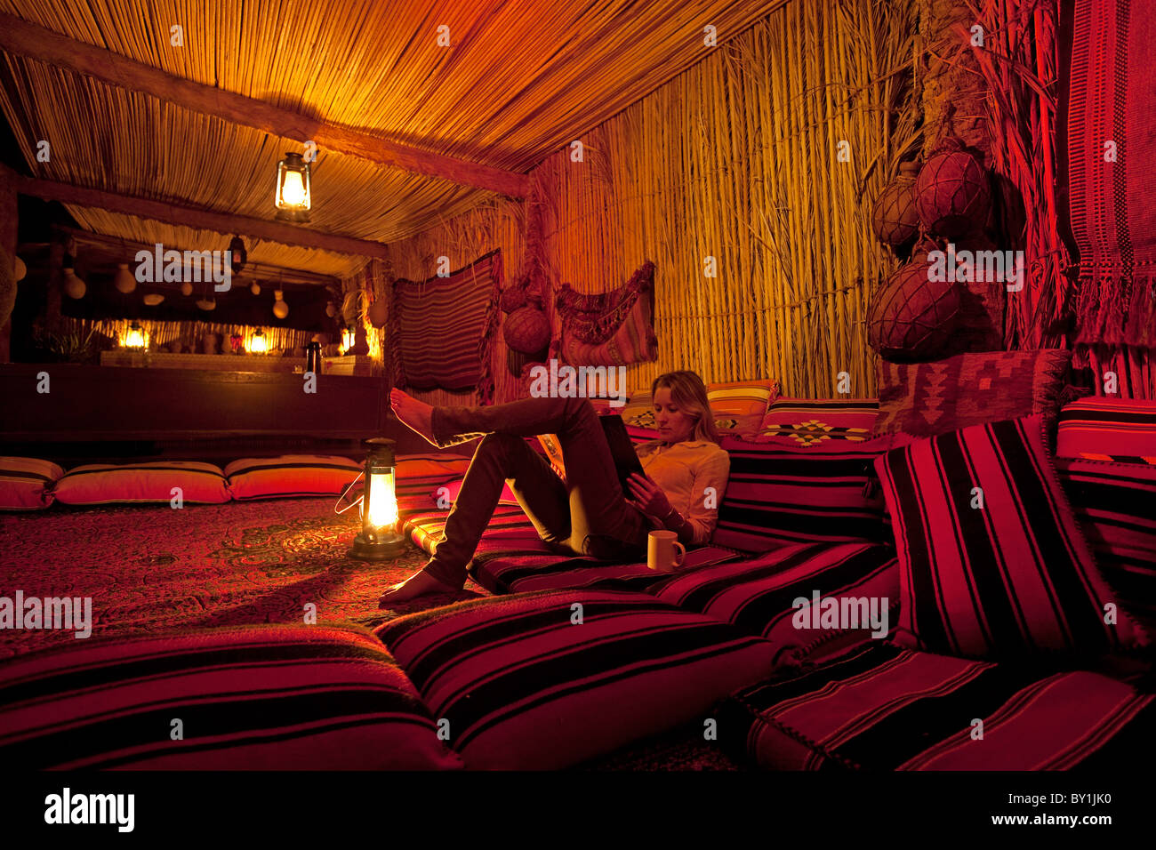 In Oman Wahiba Sands. Una giovane donna si rilassa con un libro in The Nomadic Desert Camp. Signor Foto Stock