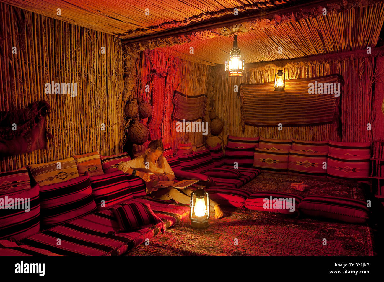 In Oman Wahiba Sands. Una giovane donna si rilassa con un libro in The Nomadic Desert Camp. Signor Foto Stock