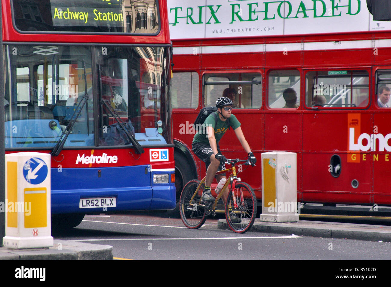 Ciclista con casco equitazione sulla corsia esterna tra due bus Foto Stock