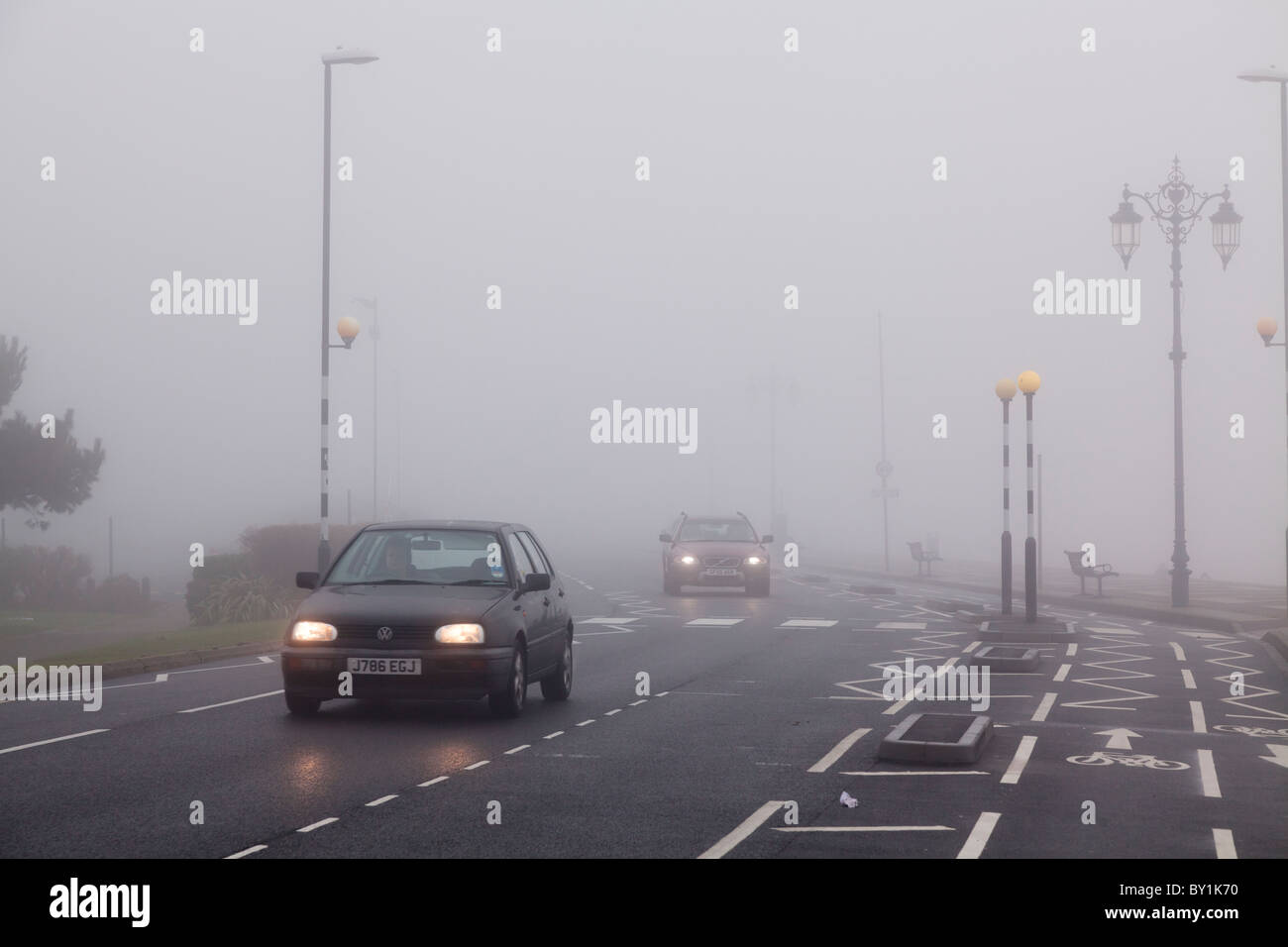 Le automobili in ambiente urbano con la segnaletica stradale orizzontale su un nebbioso giorno con luci accese Foto Stock