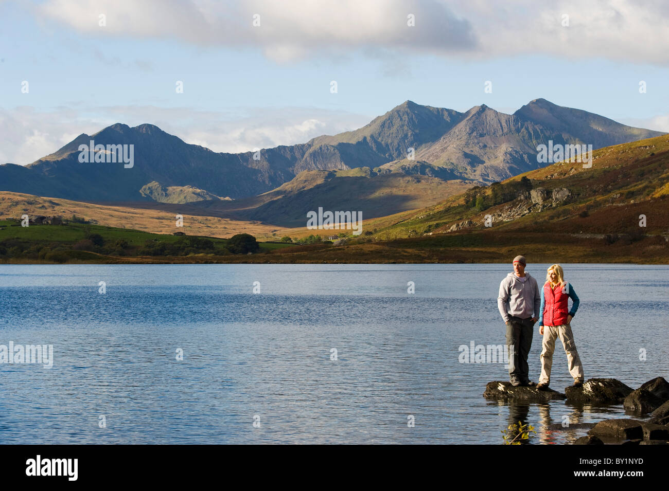 Il Regno Unito, il Galles del Nord, Snowdonia. L uomo e la donna stanno sulle rocce al bordo del Llyn Mymbyr con lo sfondo della Snowdon Foto Stock