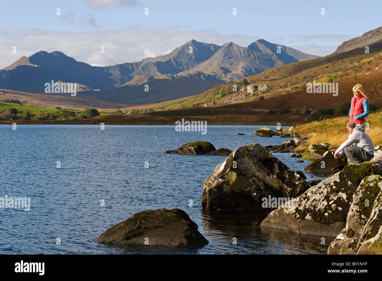 Il Regno Unito, il Galles del Nord, Snowdonia. L uomo e la donna stanno sulle rocce al bordo del Llyn Mymbyr con lo sfondo della Snowdon Foto Stock