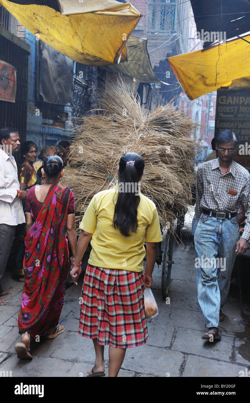 Due donne a spingere un carrello pieno attraverso le strette vie di Varanasi, India Foto Stock