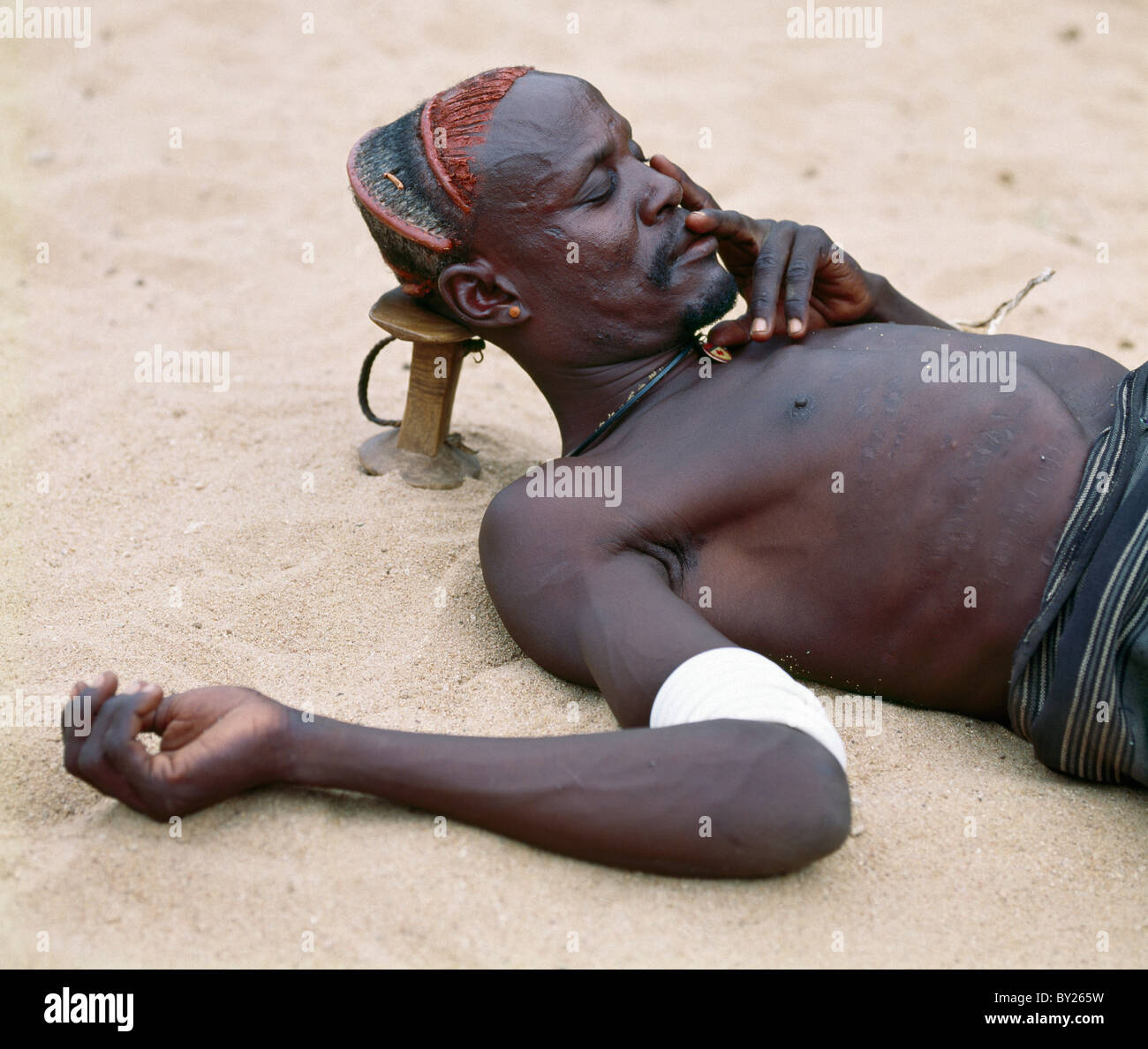 Un Turkana l uomo si prende un pisolino usando il suo sgabello in legno come un appoggiatesta per proteggere la sua elaborata acconciatura. Distretto Turkana in Kenya Foto Stock