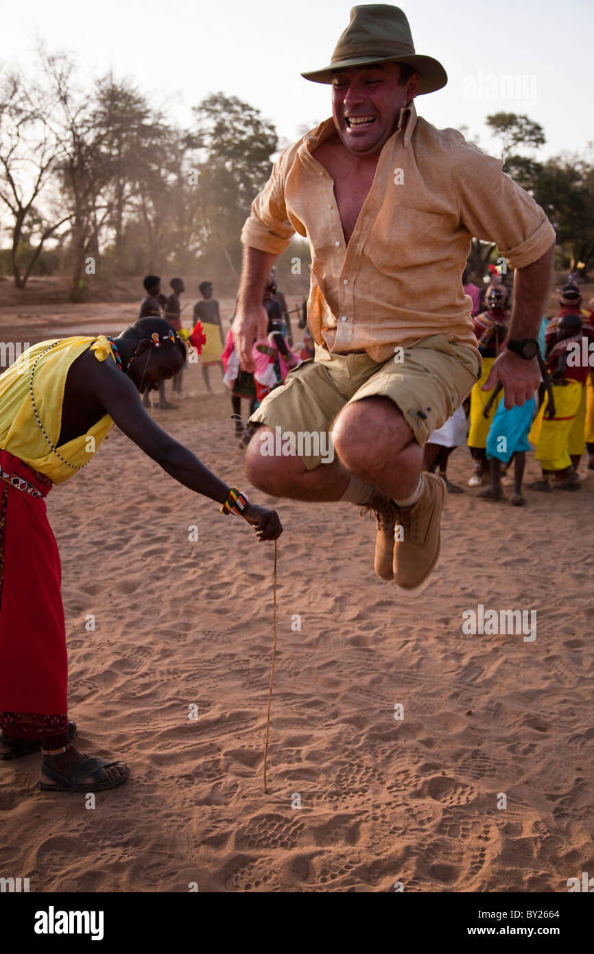 Kenya, Distretto Samburu. Un turista di tentare di saltare più in alto come un guerriero Samburu, nel letto asciutto del fiume del Ewaso Nyiro. Foto Stock