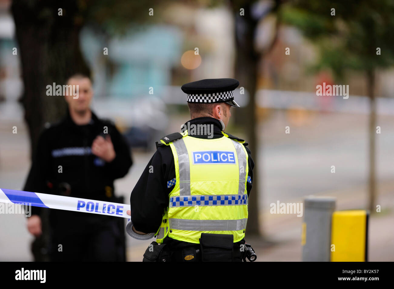Un funzionario di polizia cordoni off la scena di un incidente o di un reato utilizzando nastri di polizia Foto Stock