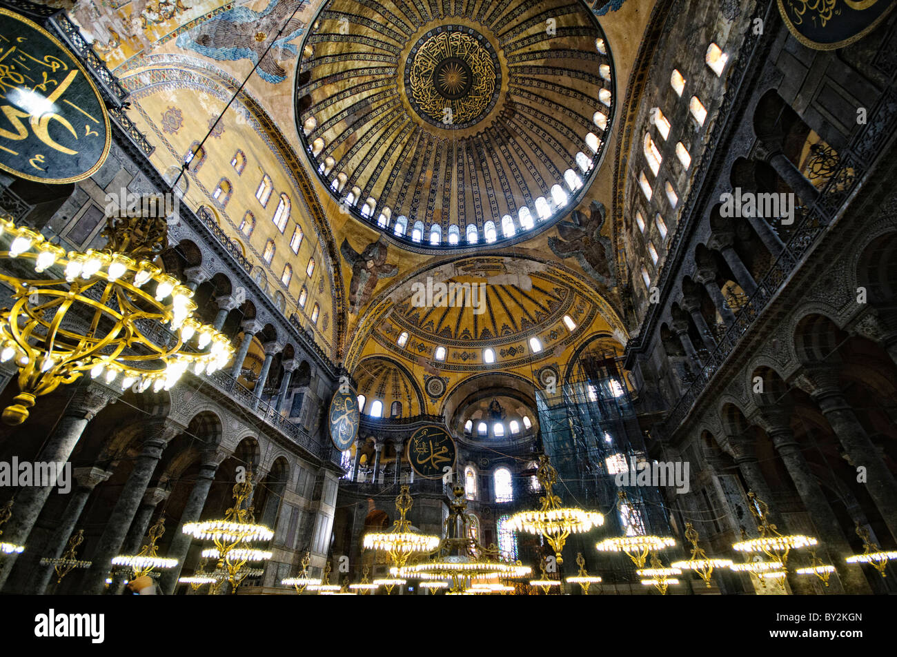 Lampadari della cupola interna di Hagia Sophia Istanbul Turchia // ISTANBUL, Turchia - la vasta sala principale di Hagia Sophia mostra il suo notevole design architettonico bizantino, con la sua imponente cupola centrale supportata da pendenti e semi-cupole. L'interno presenta elementi cristiani e islamici, tra cui mosaici bizantini, calligrafia ottomana e grandi avize ottomane (lampadari). Enormi colonne e pannelli in marmo rivestono lo spazio, dimostrando la grandezza dell'ingegneria architettonica del vi secolo. Foto Stock