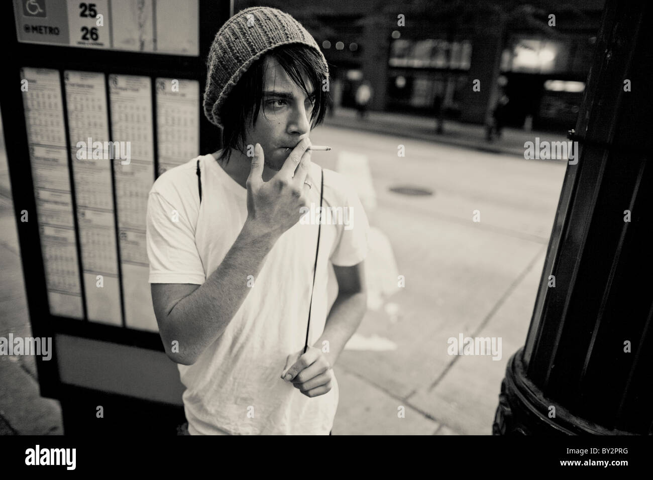 Un senzatetto giovane adulto fuma una sigaretta nel downtown di Seattle mentre è in attesa per un autobus Foto Stock