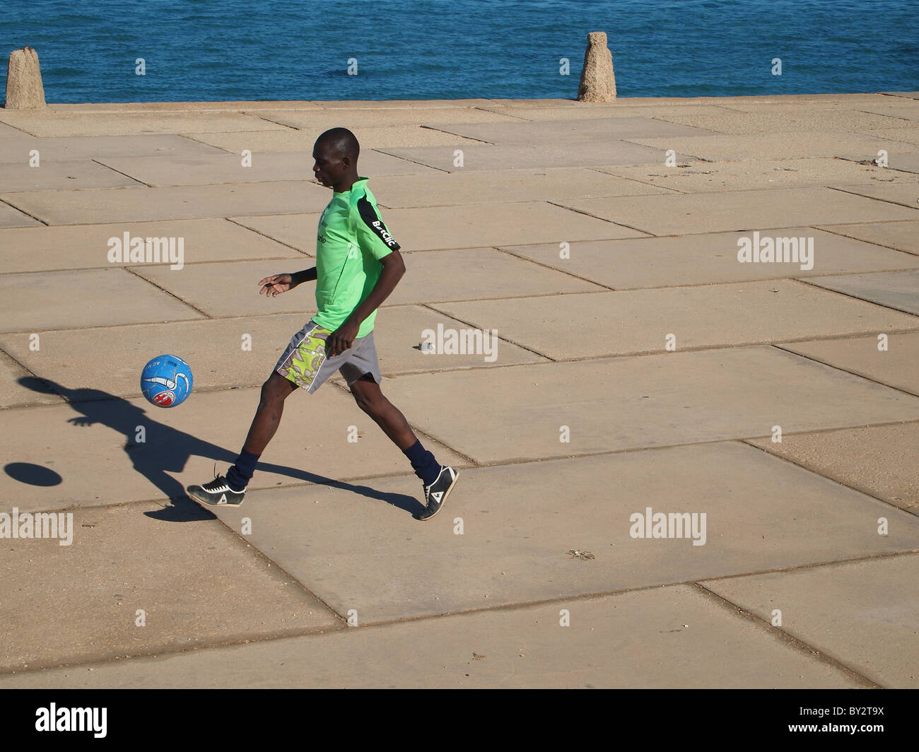 Un giovane calciatore africana di mettere in pratica le sue abilità di fronte al mare a Tripoli, Libia Foto Stock