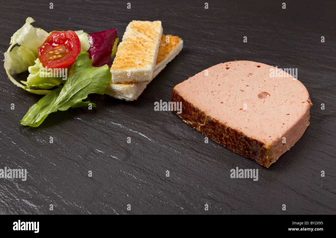 Pate Apetiser con Melba toast soldati e insalata di piccole dimensioni su ardesia scuro dello sfondo. Foto Stock