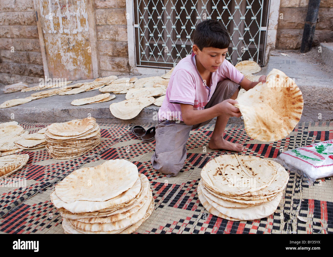 Un ragazzo siriano ordina appena sfornato-piatto di pane al di fuori di un panificio backstreet in Hama, Siria Foto Stock