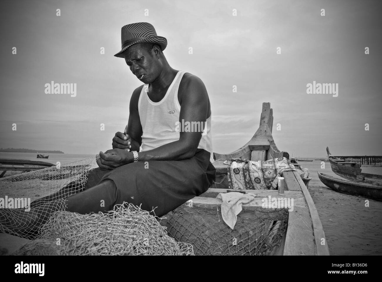 Anziano pescatore rammendo reti sulla sua barca, Sassandra, Costa d Avorio, Africa occidentale Foto Stock