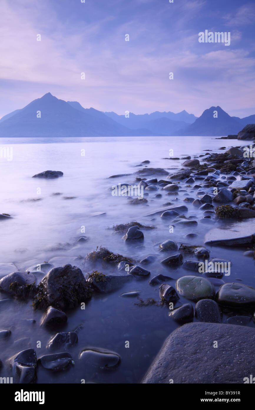 Le onde lambiscono la costa rocciosa a Elgol sull'Isola di Skye con i lontani Cuillin ridge come sfondo Foto Stock