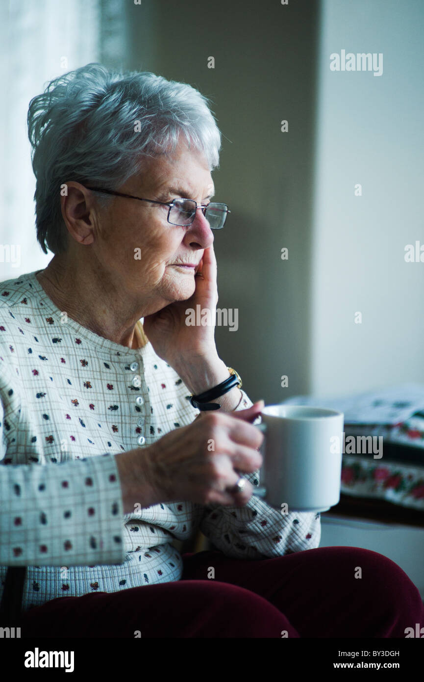 Vecchia donna con espressione preoccupata e la mano sulla faccia tenere tazza di tè. Foto Stock