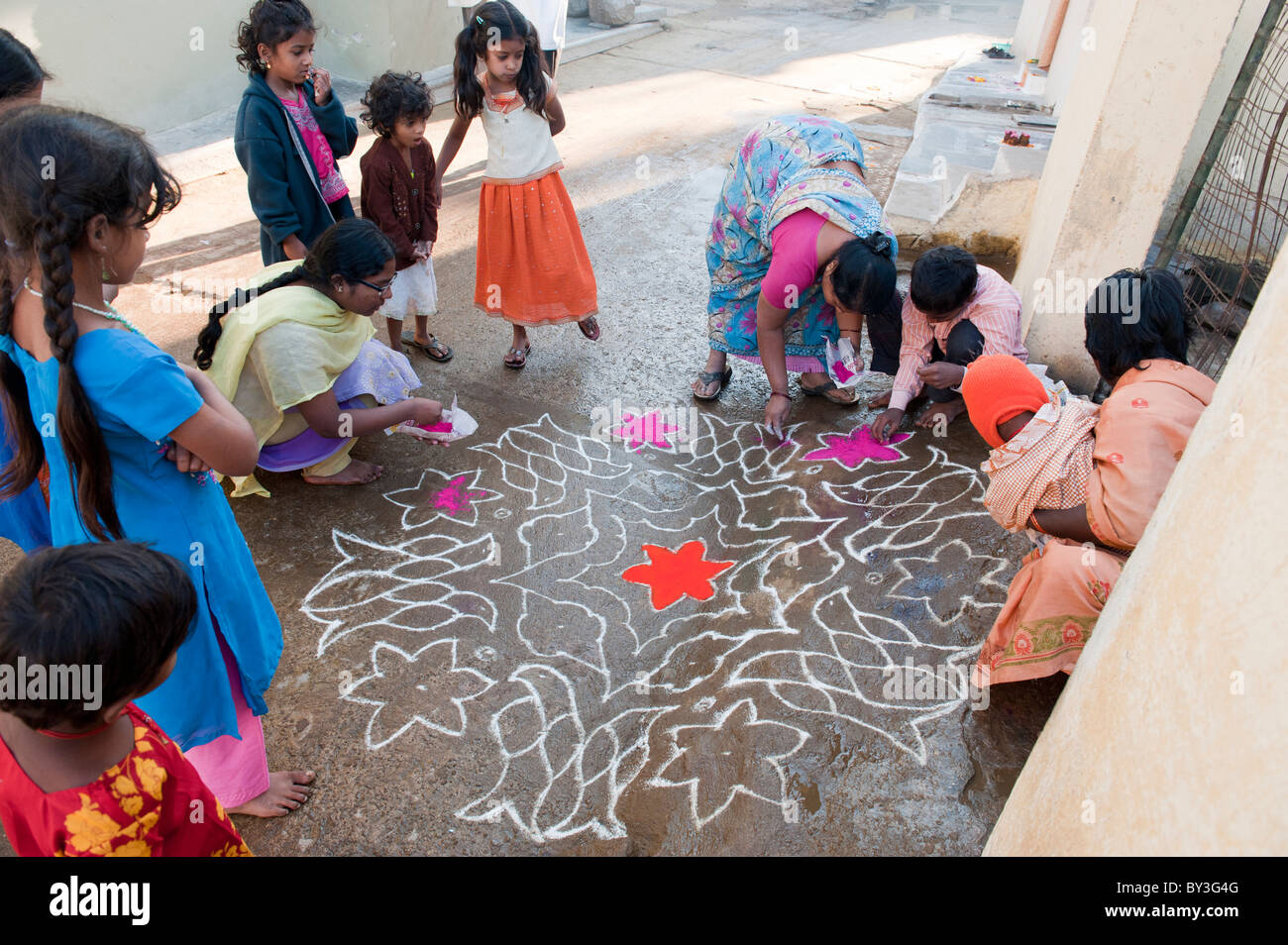 Bambini indiani guardando donne che fanno un festival sankranti rangoli design con polvere colorata per le strade di Puttaparthi, Andhra Pradesh, India Foto Stock