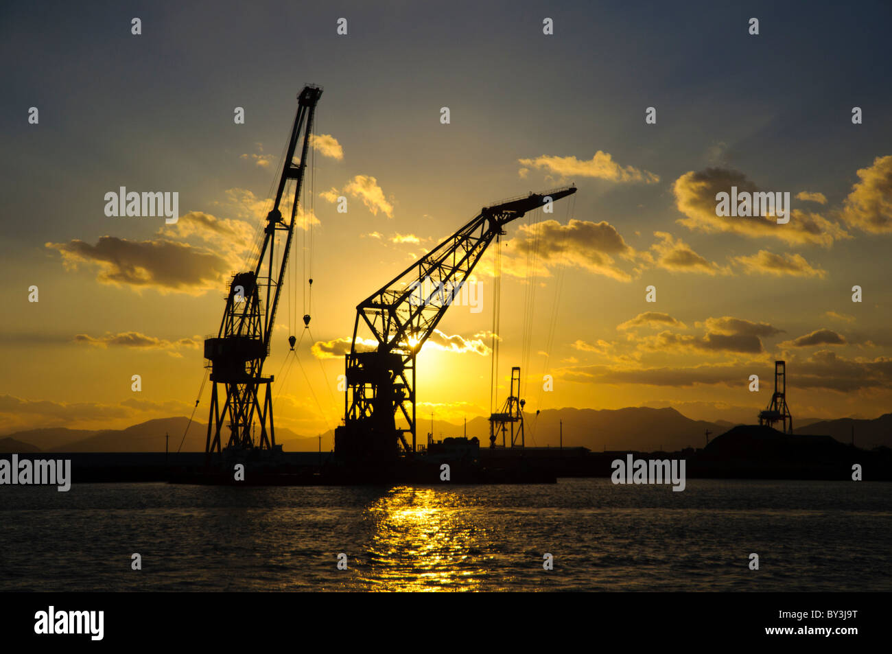 Vista al tramonto (paesaggio / seascape) di derrick gru su banchine presso un porto industriale in Asia Foto Stock