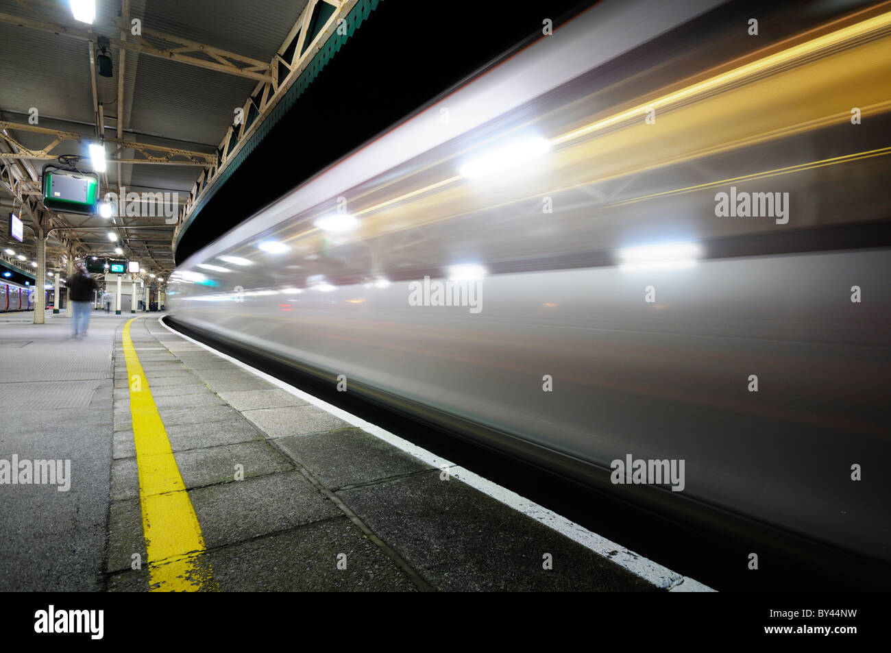Treno ad alta velocità che passa attraverso una quasi deserta stazione ferroviaria piattaforma di notte la creazione di striature di luce. Foto Stock