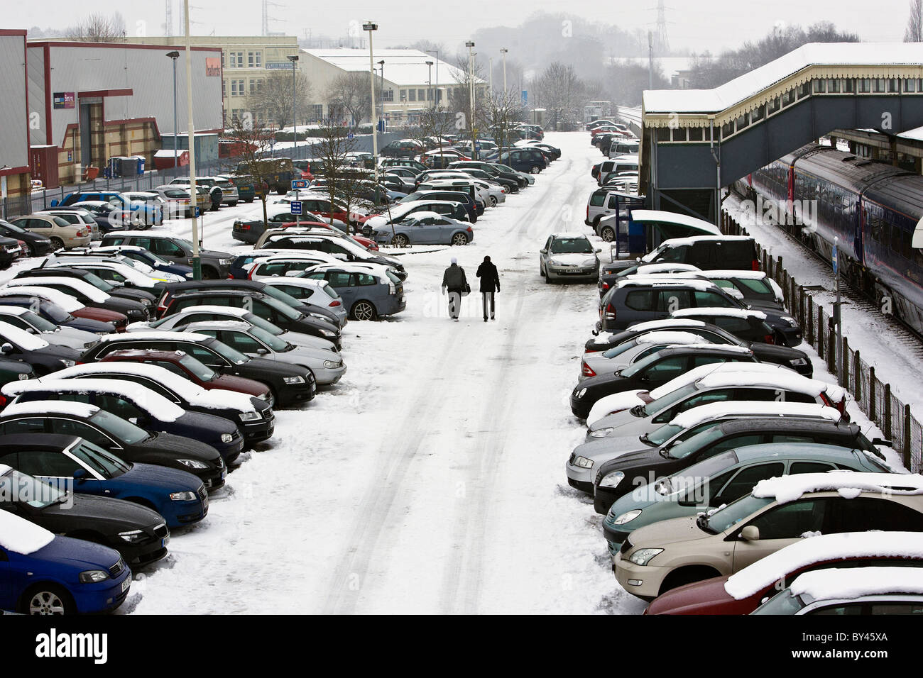 Due persone a piedi attraverso una stazione ferroviaria parcheggio auto dopo le tempeste invernali ha colpito il Regno Unito. Foto Stock