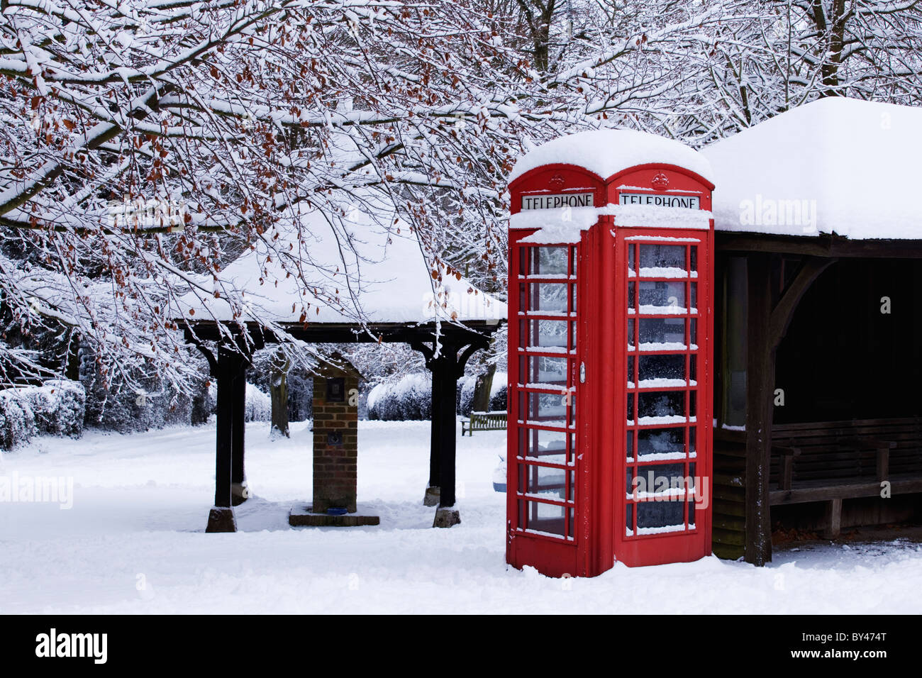 Telefono rosso scatola con neve sul villaggio inglese green Foto Stock