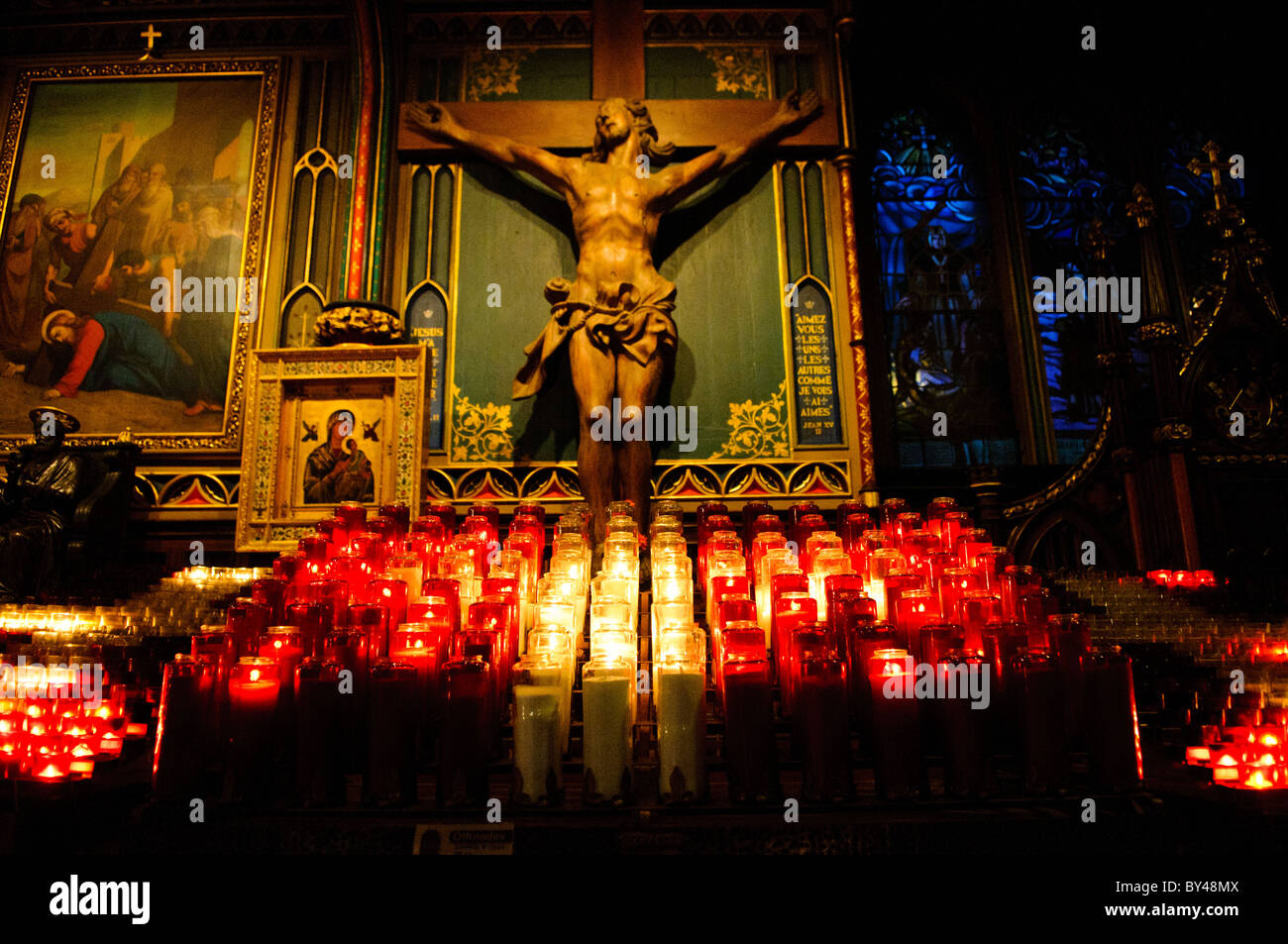 MONTREAL, Canada: Le candele votive sfarfallio davanti a un crocifisso in una cappella laterale della basilica di Notre-Dame di Montreal, costruita a metà del XIX secolo. L'intimo spazio devozionale presenta decorazioni ornamentali in stile neogotico caratteristico dell'interno della basilica. Questa cappella esemplifica i tradizionali spazi devozionali cattolici che si trovano in tutta la chiesa storica, che serve sia come luogo di culto attivo che come principale destinazione turistica. Foto Stock