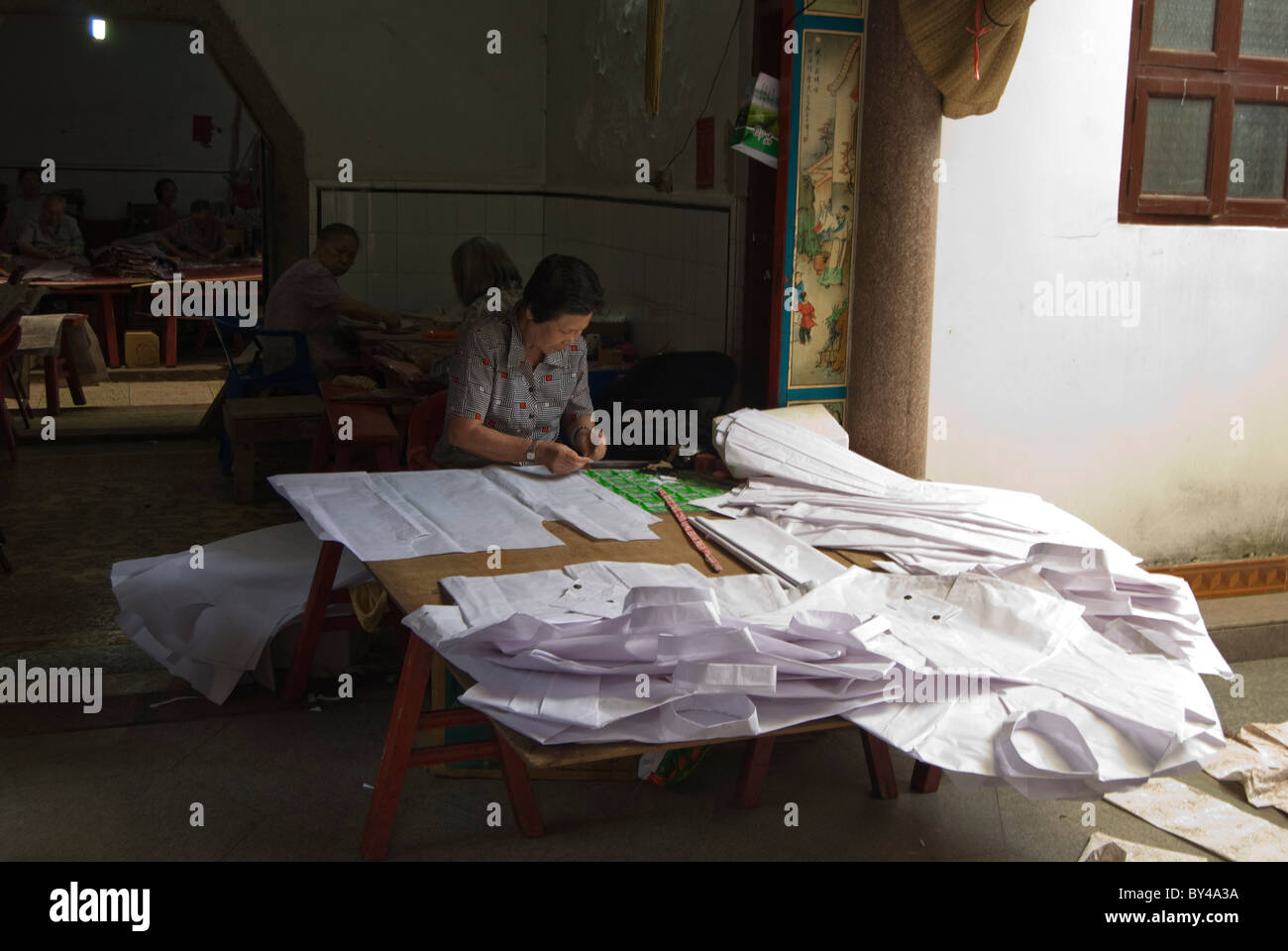 Una donna cinese è la preparazione di carta vestiti per la vita dopo la morte in un santuario a Shantou. Foto Stock