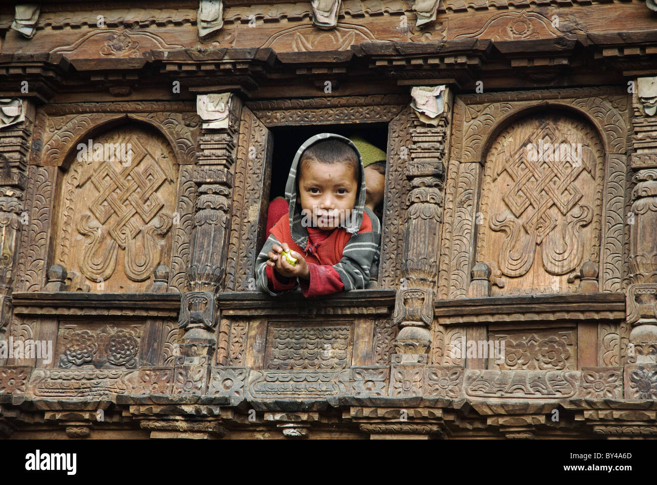 Un ragazzo Tamang orologi da una finestra in una riccamente intagliati casa in legno, Gatlang, Tamang Heritage trek, Nepal Foto Stock