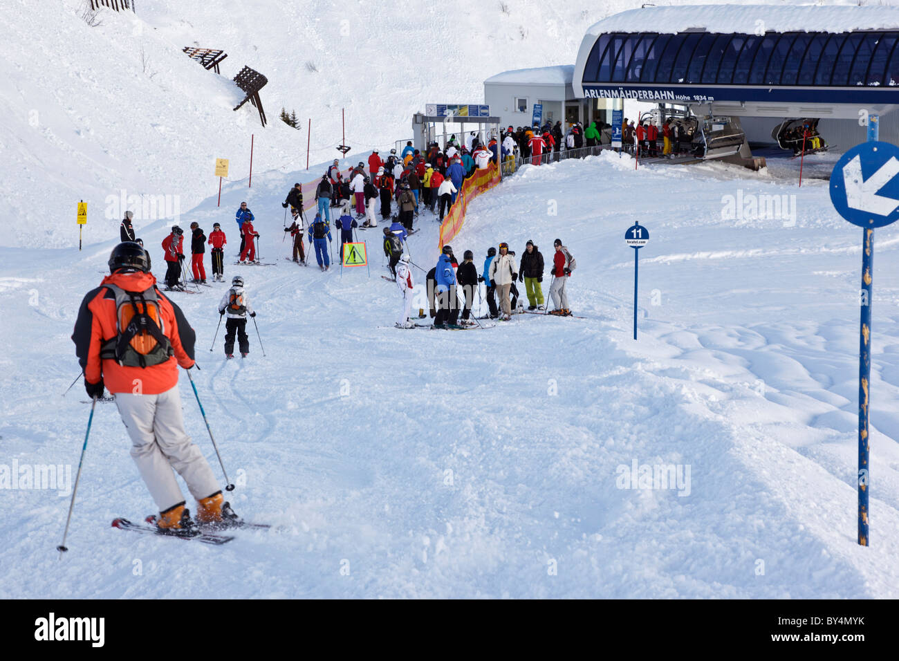 Gli sciatori e gli snowboarder la giunzione di una coda per ottenere sulla seggiovia Arlenmahder in Austrian ski resort di St Anton. Foto Stock