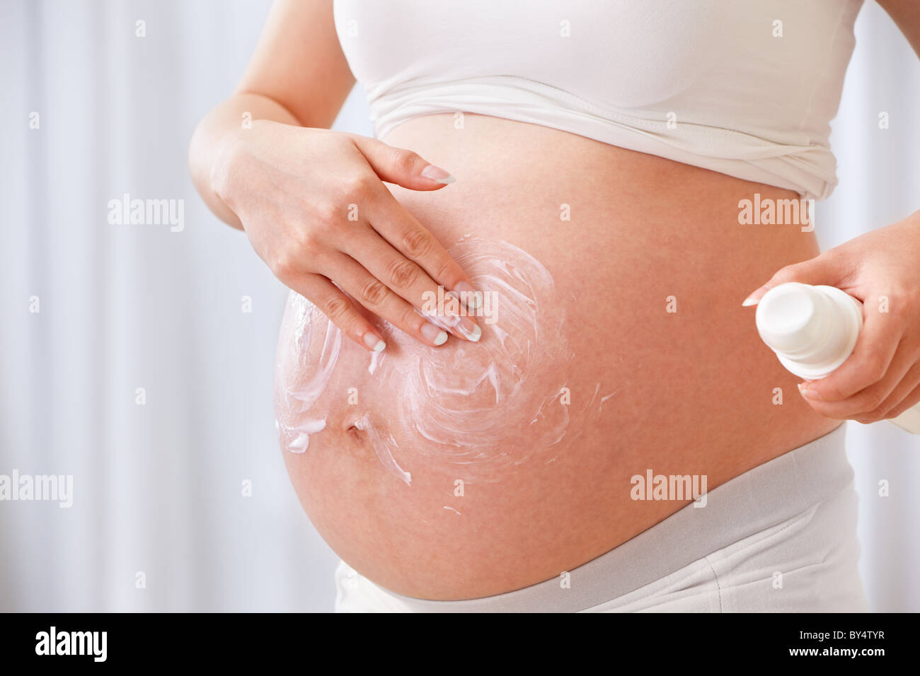 Macchie di crema di umidità sul ventre della donna incinta su bianco Foto Stock