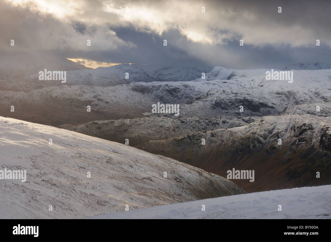 Vista da Dollywagon luccio in inverno nel Lake District inglese. Rompere il cloud e i raggi di luce del sole verso Harrison Stickle Foto Stock