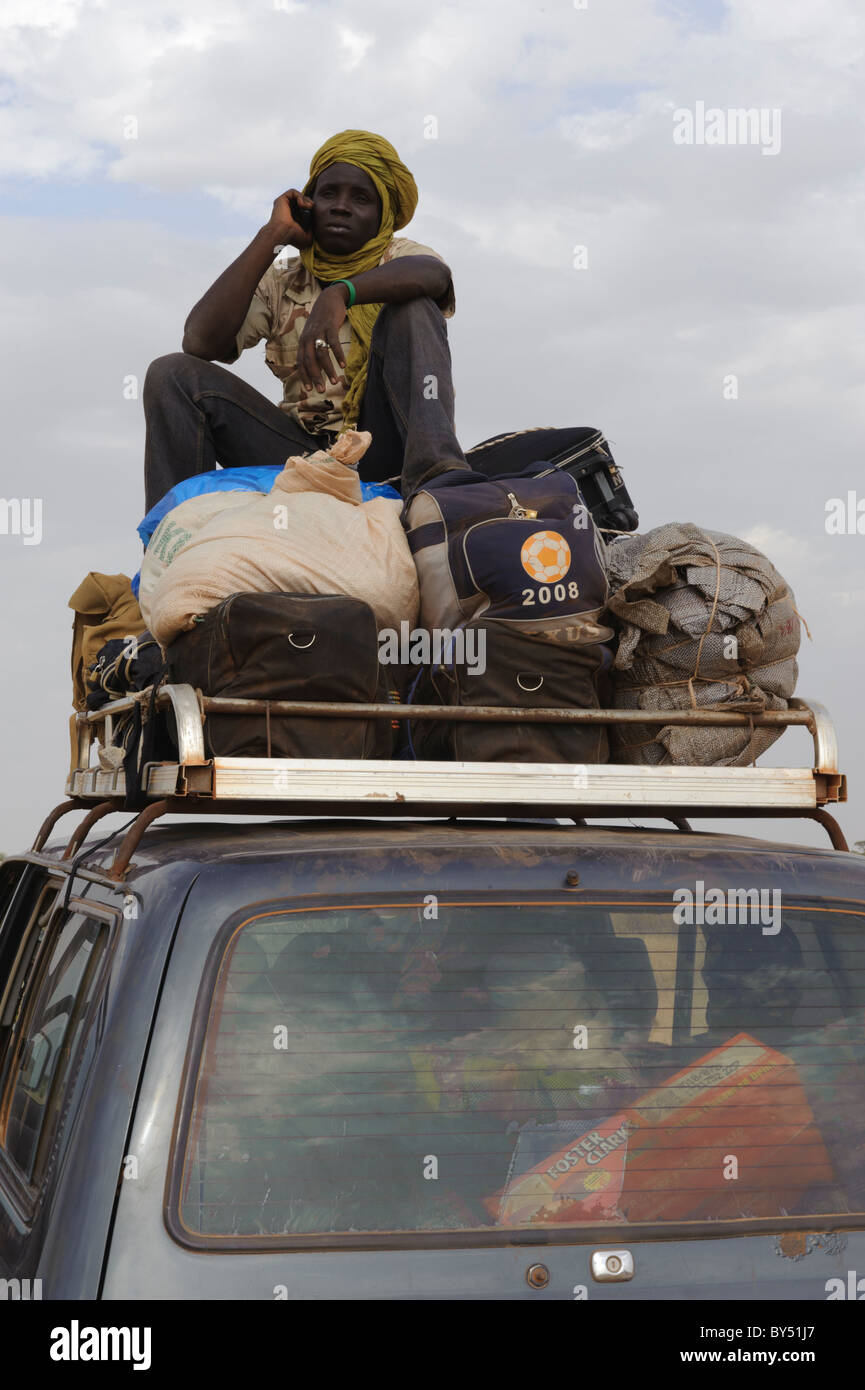 Touareg uomo seduto sui bagagli sulla parte superiore di un 4X4 utilizzando il suo cellulare mobile. Regione Gourma, Mali. Foto Stock