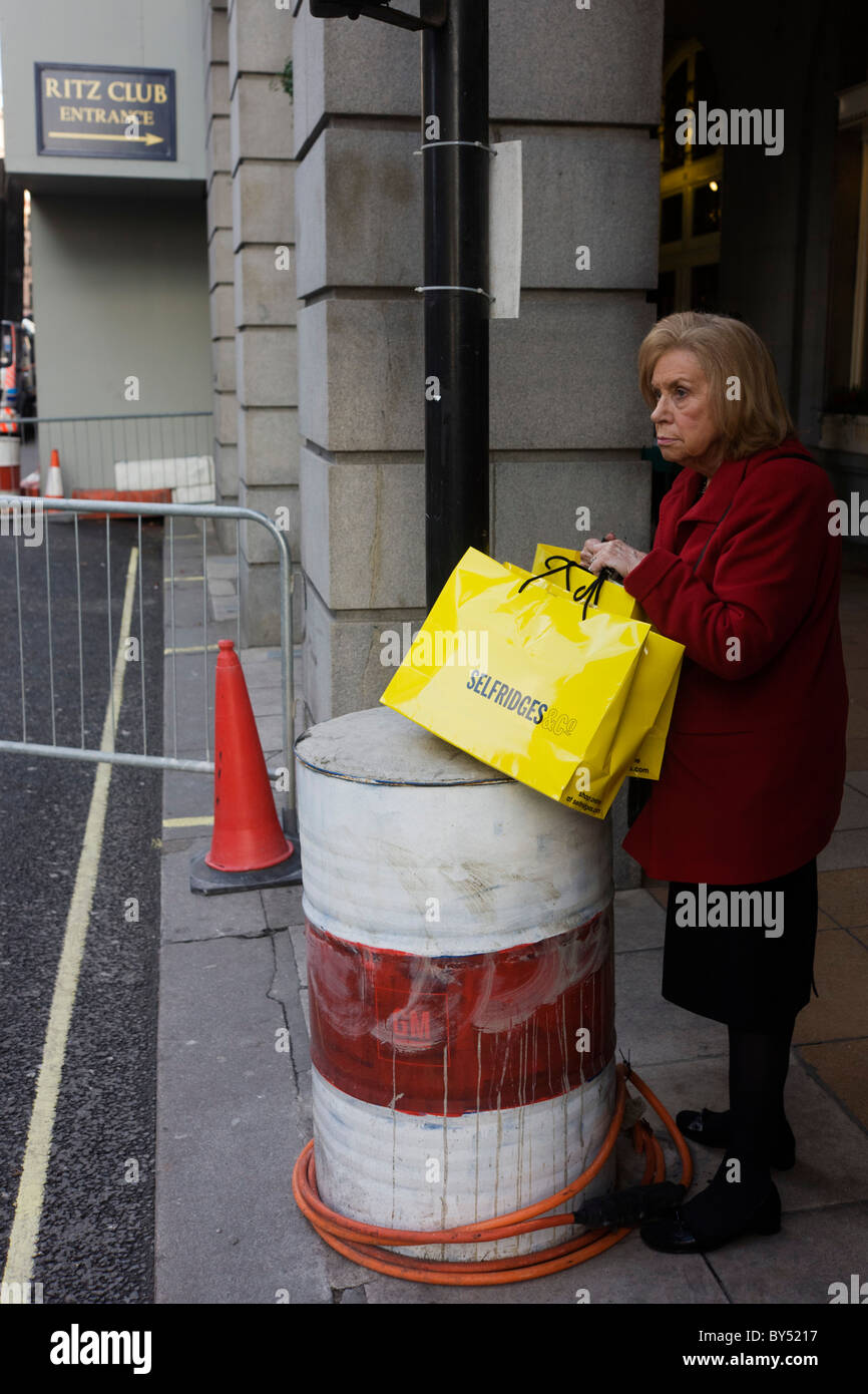 Una signora con una dal grande magazzino Selfridges shopping bags sorge dalla vecchia costruzione tamburo di petrolio al di fuori del Ritz lavori stradali. Foto Stock