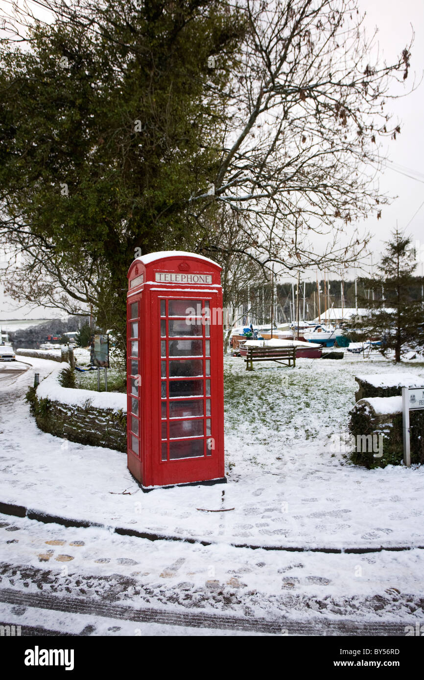 Un telefono rosso kiosk nella neve a Gweek, Cornwall Foto Stock