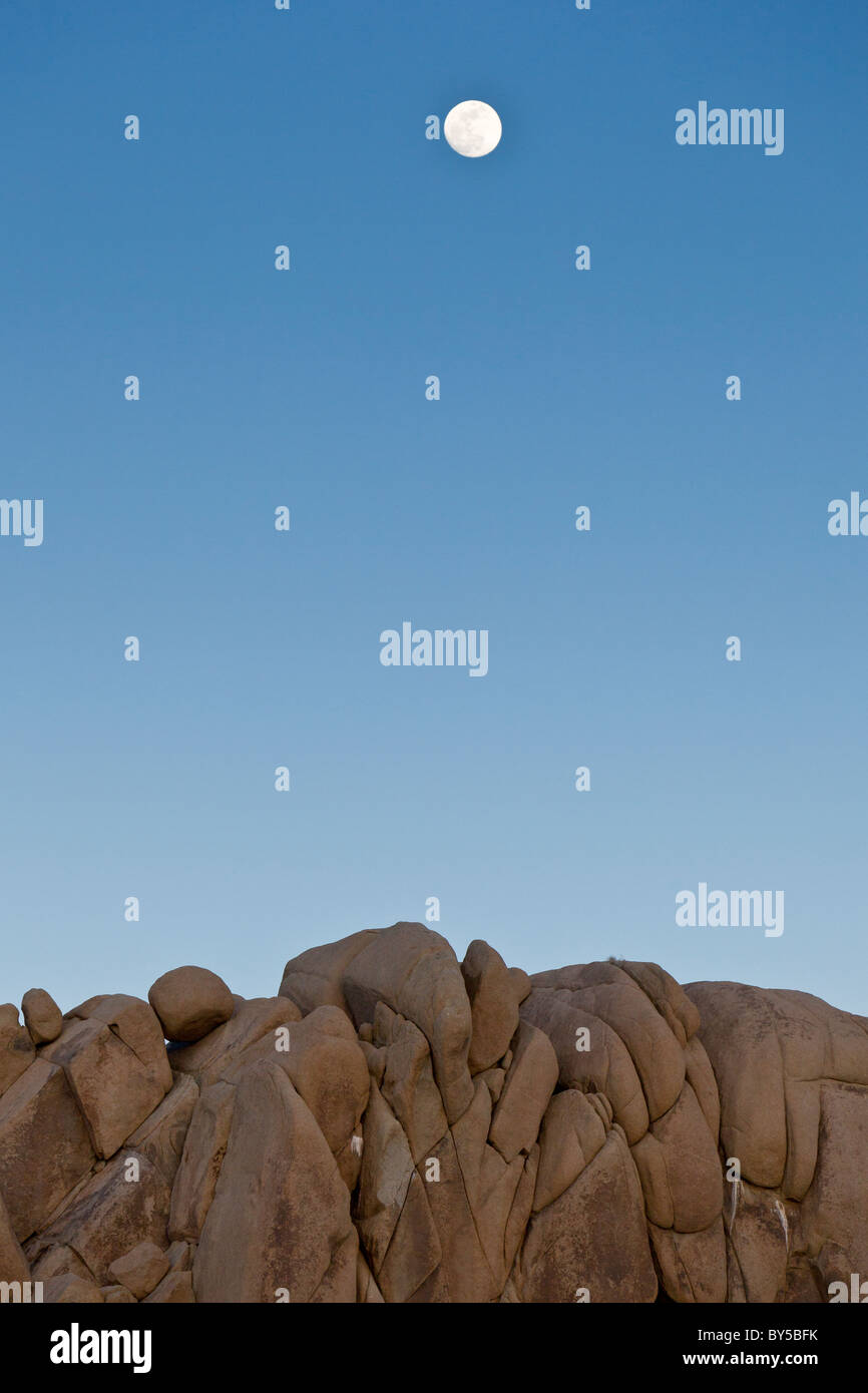 La luna piena si libra sul granito surreale formazioni rocciose al tramonto a Joshua Tree National Park, California, Stati Uniti d'America. Foto Stock